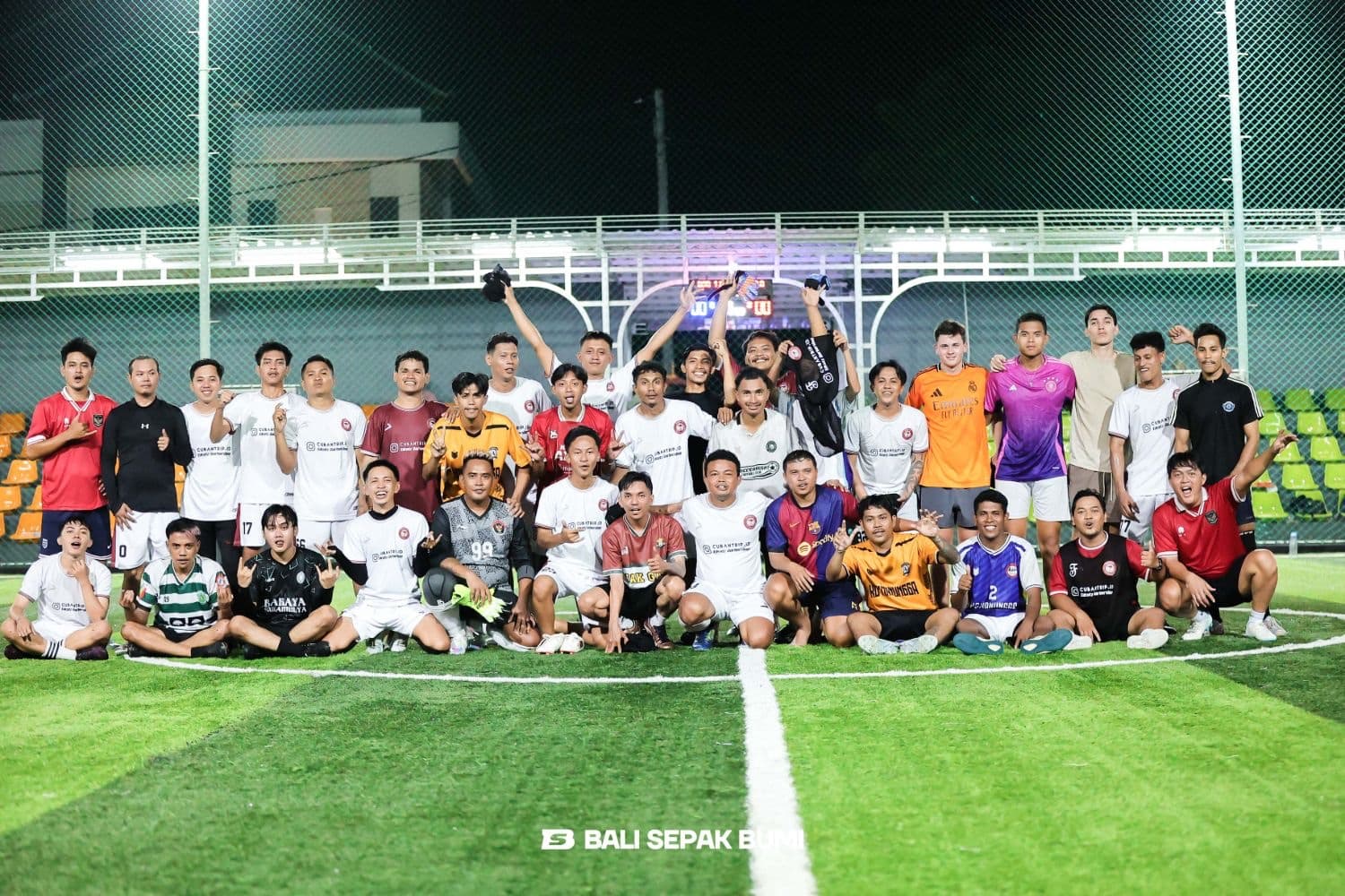 A large group of men posing together on a football pitch at night