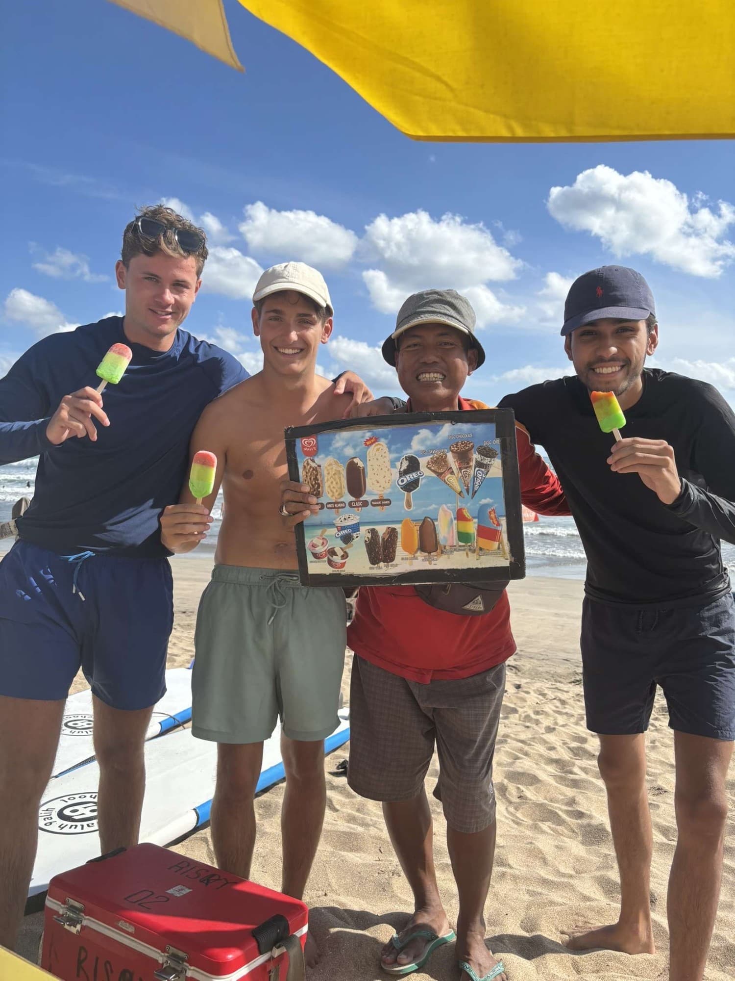 The ice cream seller, with three young men enjoying ice creams on the beach