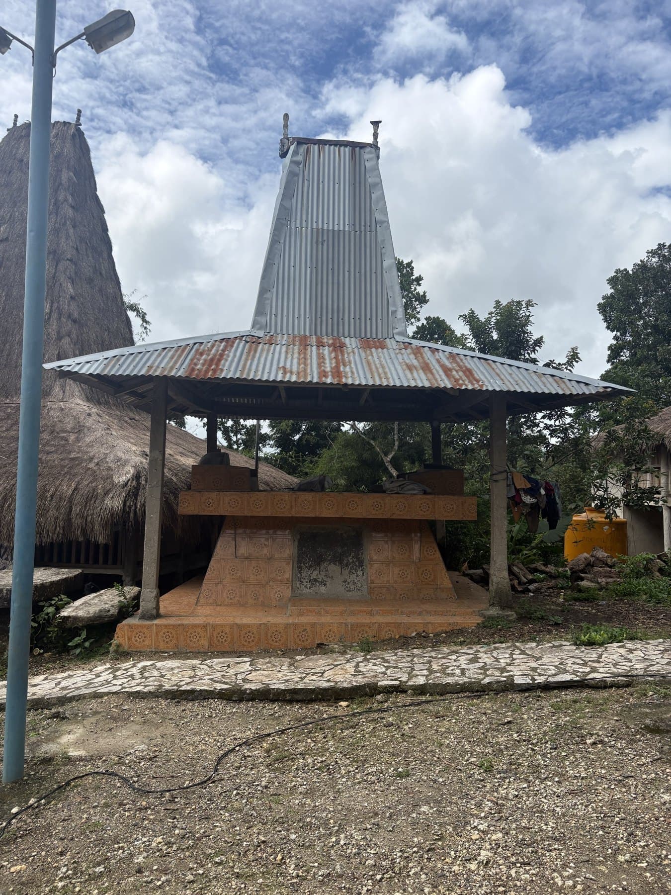 A tiled grave under a roof next to traditional thatched houses on Sumba
